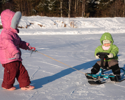 Ребенок тянет другого на снегокате