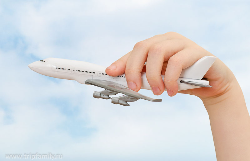 Child hand holding model airplane on sky background.
